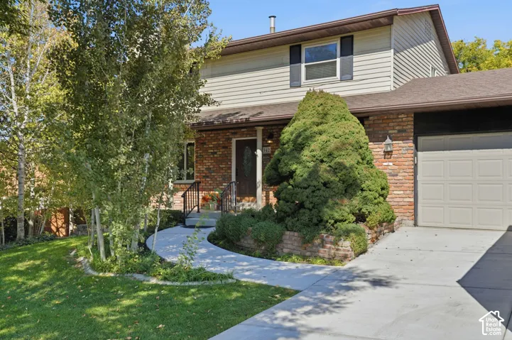 Multi-level exterior featuring a brick and horizontal siding facade, attached garage, concrete driveway, and a paved walkway leading to the entrance