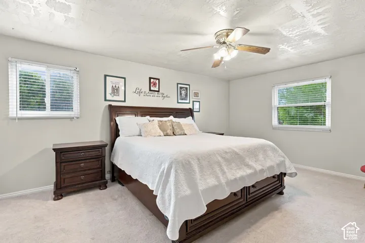 Room featuring neutral wall tones, two dual-pane windows, wall-to-wall carpeting, and a ceiling-mounted fan with integrated lighting