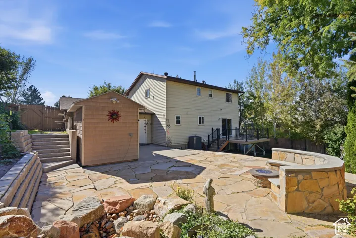 Flagstone patio featuring a built-in stone fire pit and curved stone bench, tiered concrete stairs, and elevated wood deck with metal railings