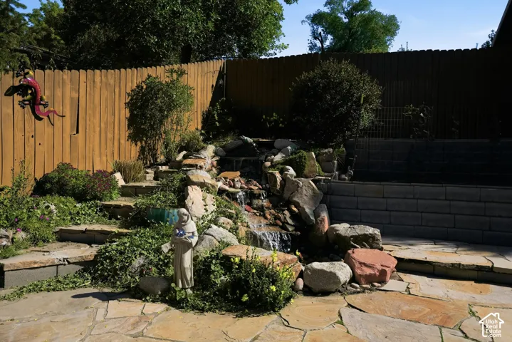 Backyard featuring natural stone patio, tiered rock water feature, segmented concrete block retaining wall, and wood privacy fencing
