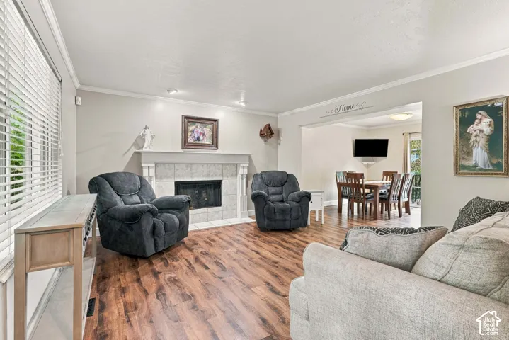 Living area featuring wood-finish flooring, a fireplace with tile surround, crown molding, and recessed lighting