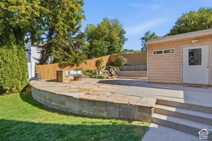 Backyard featuring a multilevel stone patio, decorative rock water feature, wood-shingle exterior outbuilding, concrete stairs, and perimeter wood fencing