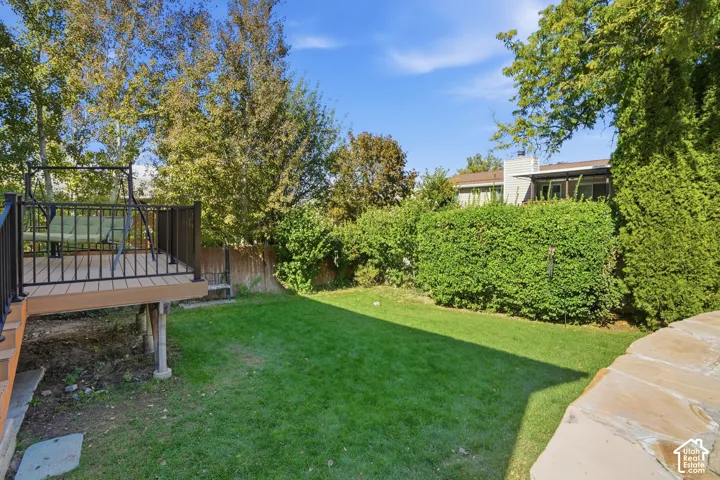 Backyard featuring a composite deck with metal railing, stone-finished retaining wall, and mature landscaping