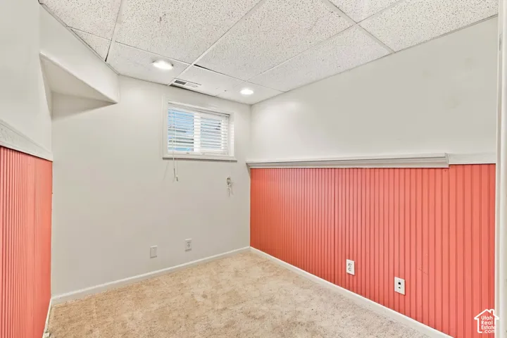 Interior space featuring wall-to-wall carpeting, beadboard wainscoting, a drop ceiling with recessed lighting, and a window with blinds