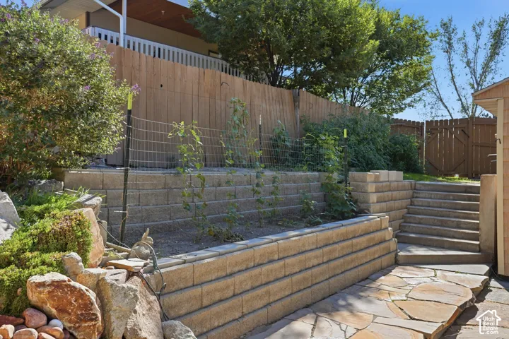 Terraced landscaping featuring segmented concrete block retaining walls, natural stone hardscaping, tiered planting beds, and wood privacy fencing
