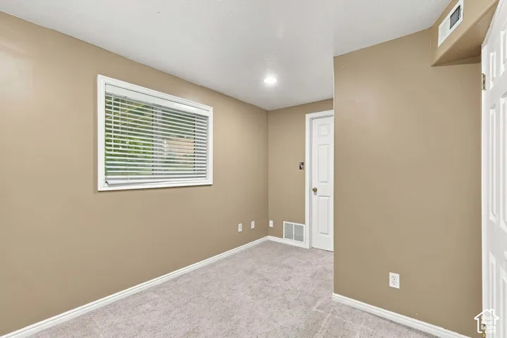 Neutral-toned interior room featuring wall-to-wall carpeting, a multi-pane window with horizontal blinds, recessed ceiling lighting, and a six-panel interior door