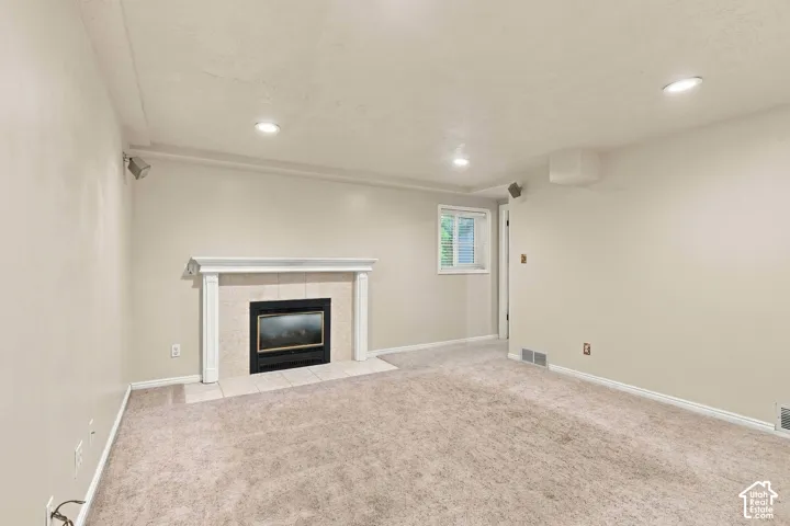 Fireplace with a classic white mantel, tile hearth, recessed lighting, and neutral carpeting