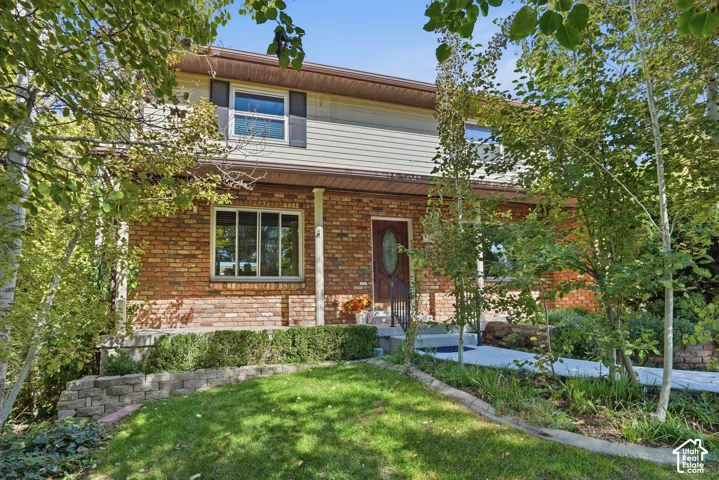 Two-story exterior featuring a brick and horizontal siding facade, covered front porch, decorative glass entry door, and stone retaining wall