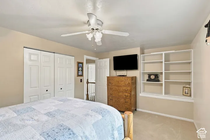 Room featuring wall-to-wall carpeting, built-in shelving, white multi-panel closet doors, and a ceiling fan with integrated light fixture