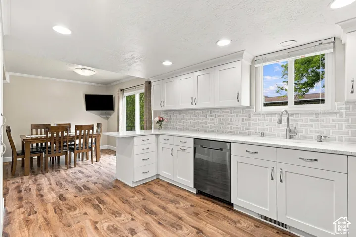 Kitchen featuring white Shaker cabinetry, quartz countertops, a stone-tile backsplash, stainless steel dishwasher, and wood-finish flooring