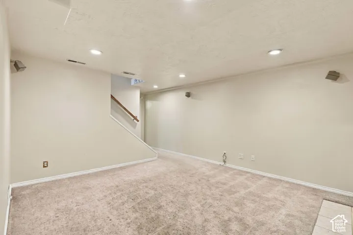 Neutral-toned carpeting, recessed ceiling lighting, and a staircase featuring a wooden handrail