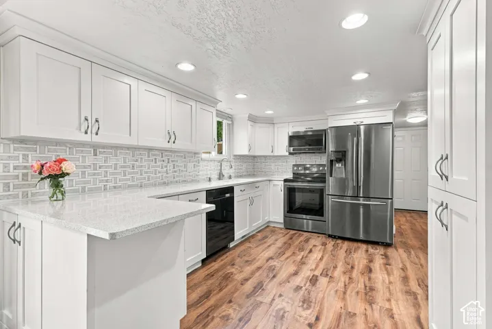 Kitchen featuring white shaker-style cabinetry, light stone-finish countertops, subway tile backsplash, wood-finish flooring, and recessed ceiling lighting
