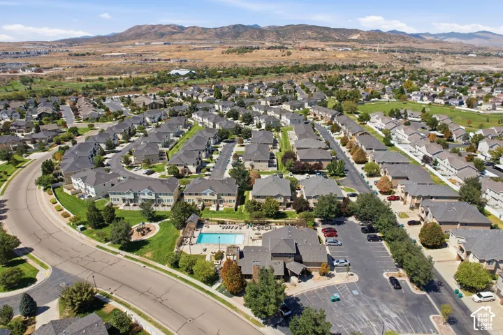 Aerial perspective of a residential community featuring a swimming pool, paved parking areas, curated landscaping, and a mountainous backdrop