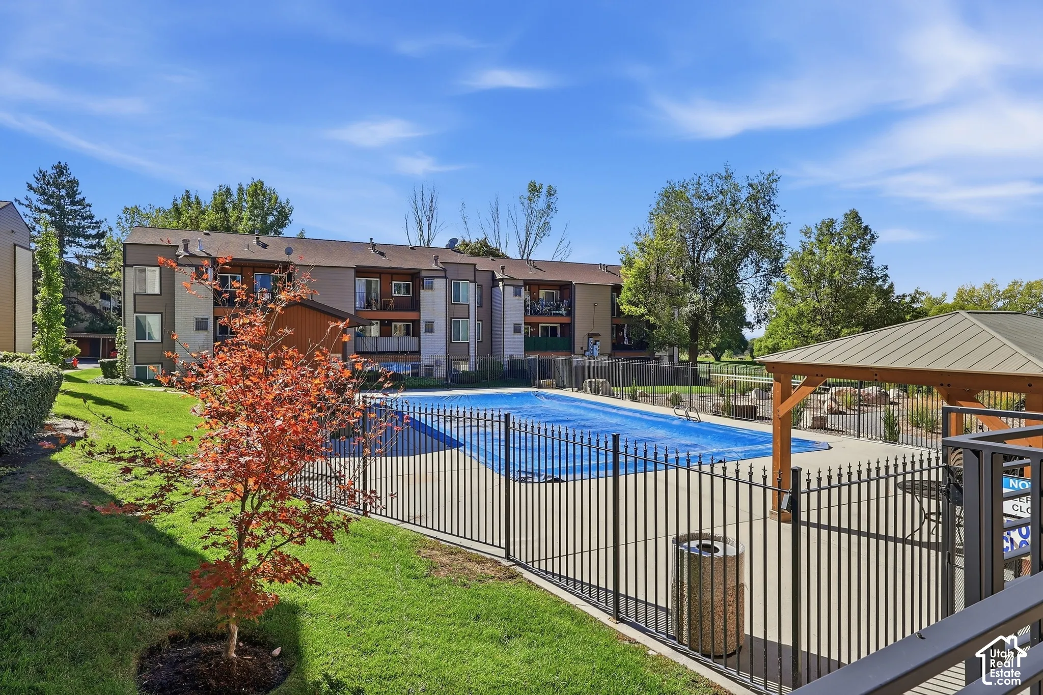Outdoor pool area featuring a metal fence, surrounding concrete patio, and a covered gazebo structure