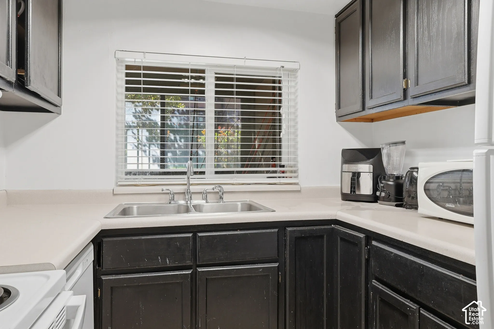 Kitchen featuring dark-finish cabinetry, light-toned countertops, and a double basin stainless steel sink with a chrome faucet
