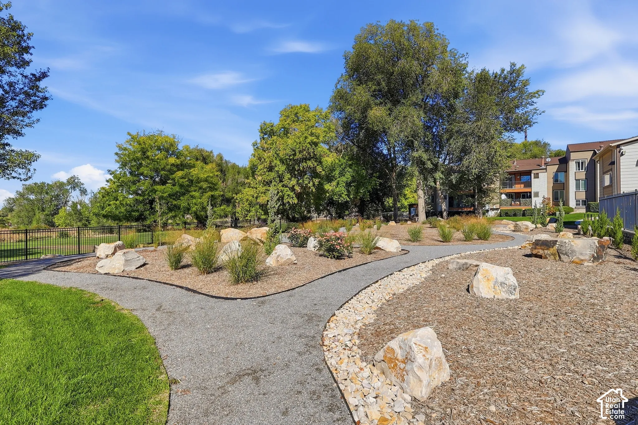 Gravel pathways winding through a landscaped area featuring decorative boulders, low-lying shrubs, and mature trees