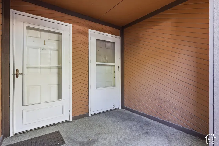 Entryway featuring a white storm door, brown textured siding, and a concrete floor