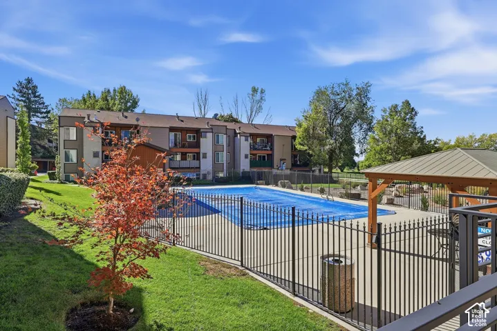 Outdoor pool area featuring a metal fence, surrounding concrete patio, and a covered gazebo structure