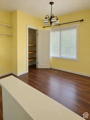 Wood-finish flooring, built-in shelving, window with blinds, and an overhead chandelier