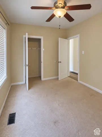Carpeted room featuring a ceiling fan with integrated lighting, a window with blinds, and two doorways