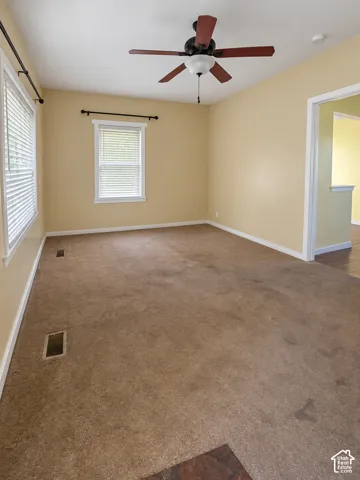 Carpeted room with a ceiling fan with light fixture, multiple windows, and light-colored walls