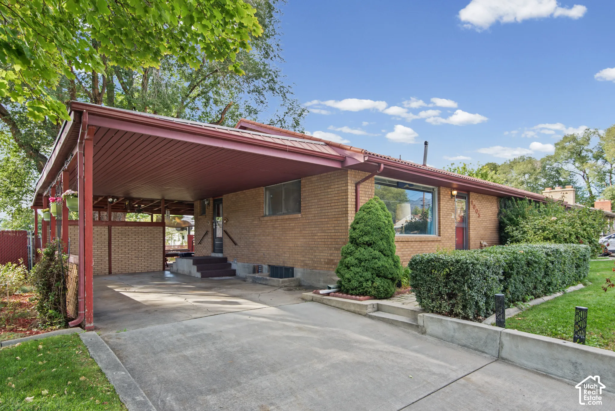 Brick exterior with an attached carport, covered entry, front door, and established landscaping