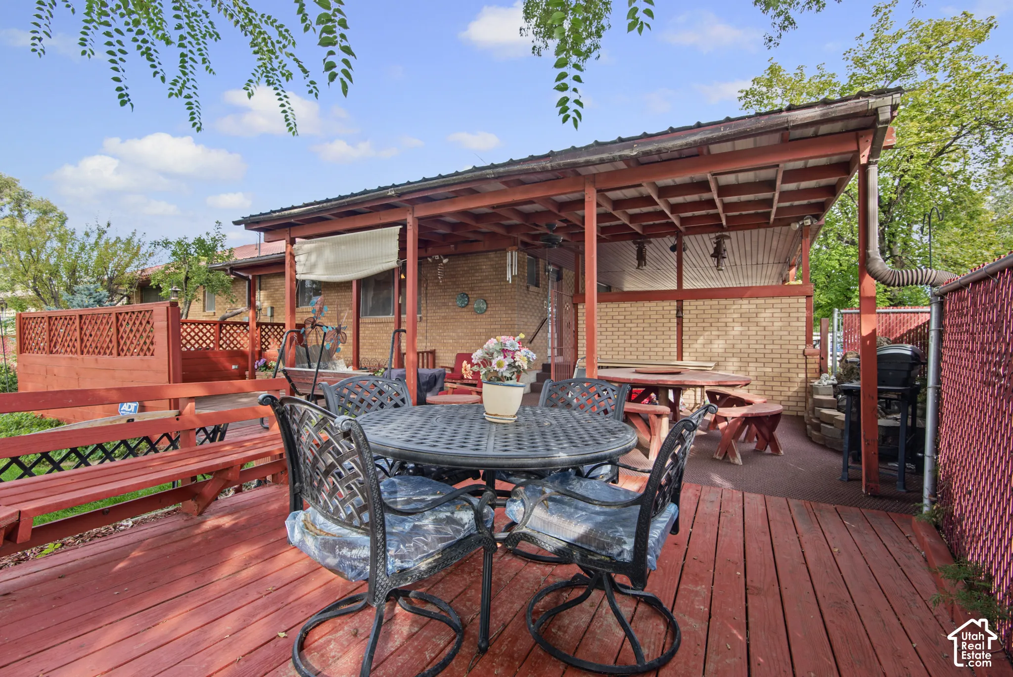 Expansive wooden deck featuring a built-in bench, covered patio, and brick exterior