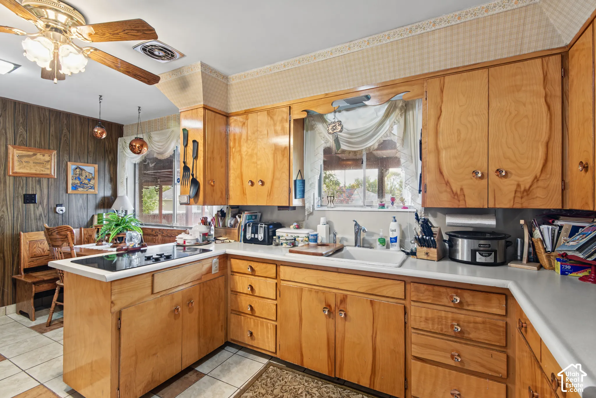 Kitchen featuring wood-finish cabinetry, integrated cooktop, ceiling fan, and a window above the sink