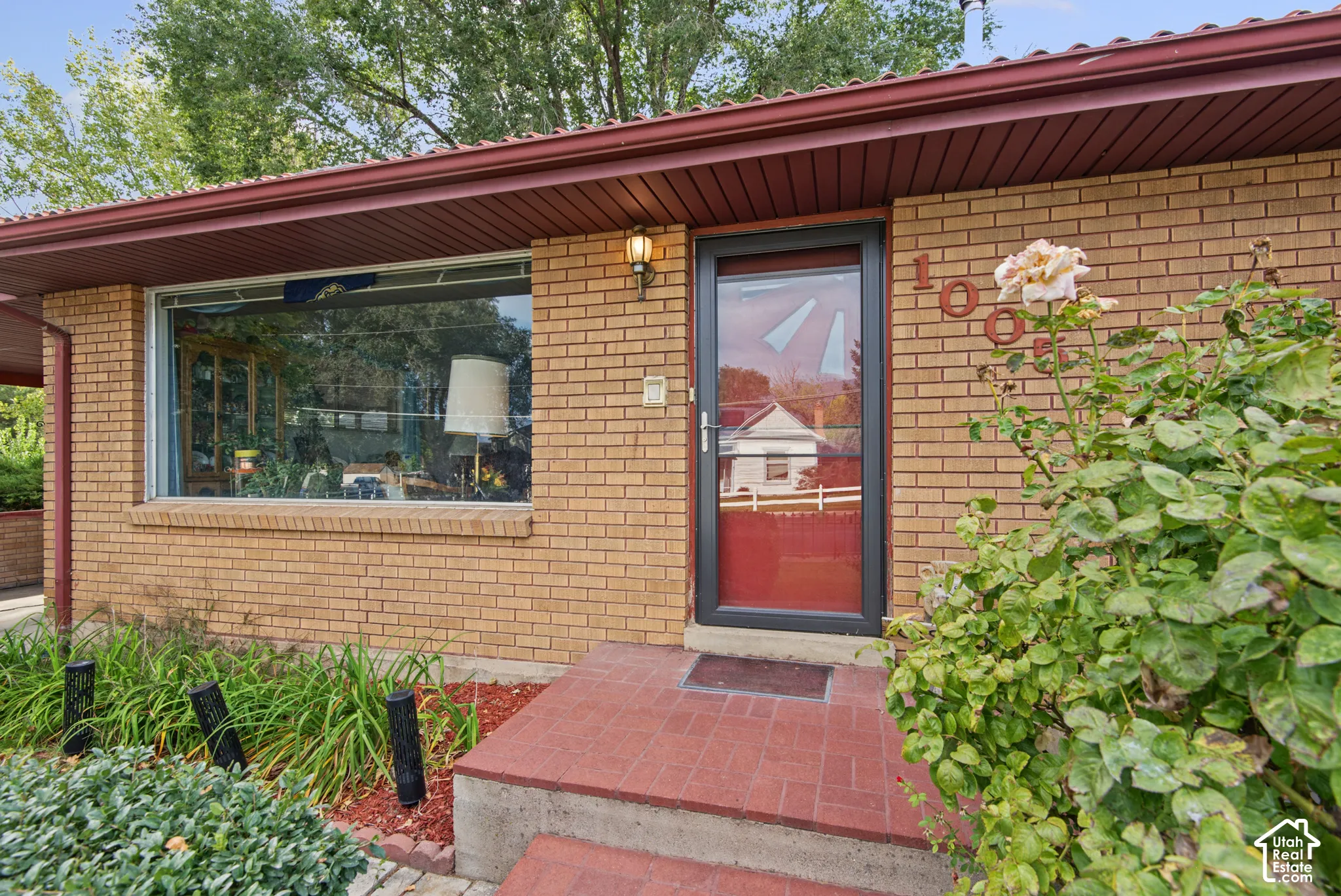 Brick exterior with large picture window, red screen door, and exterior sconce lighting