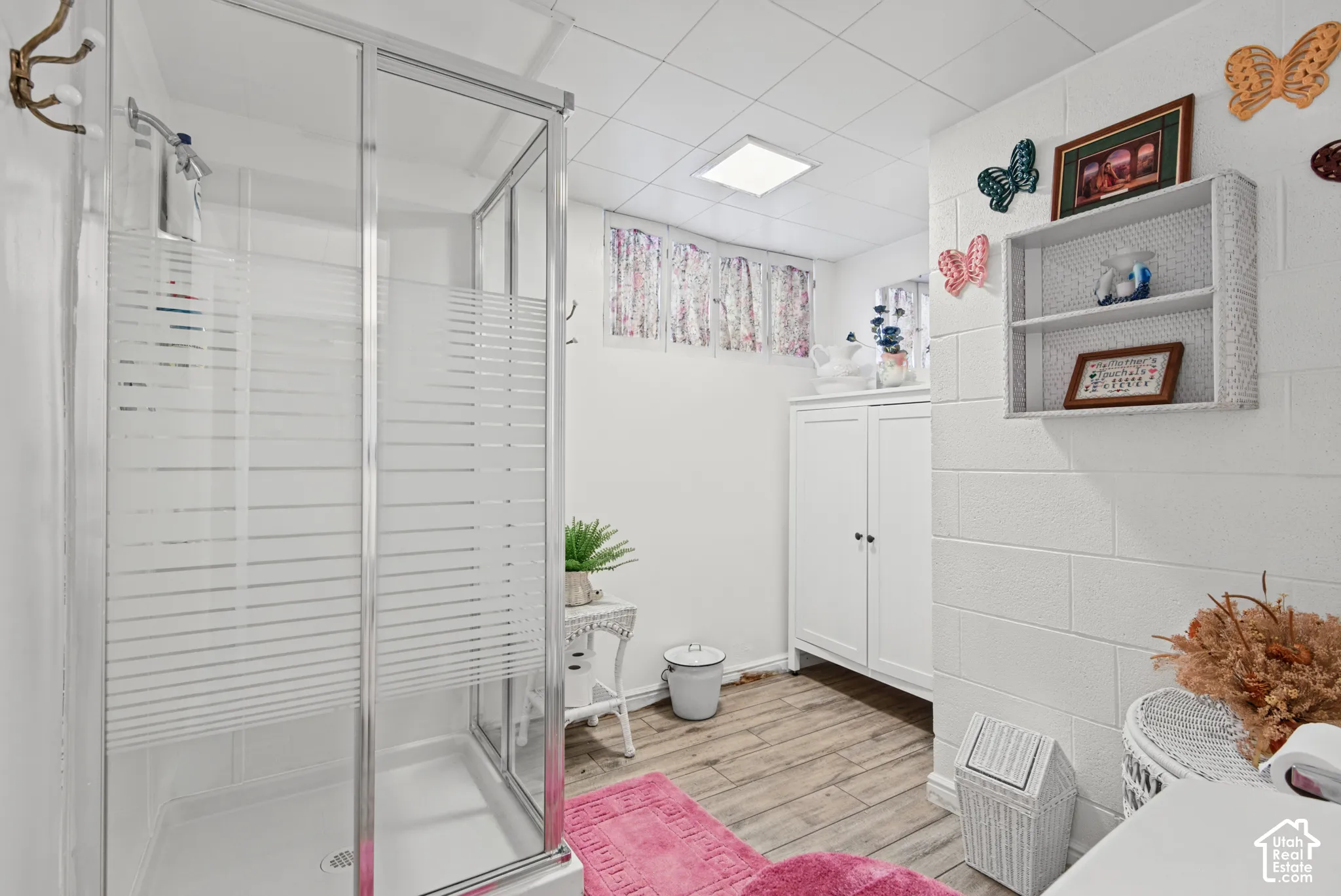 Enclosed shower with frosted glass, wood-finish flooring, white built-in cabinetry, and white block walls