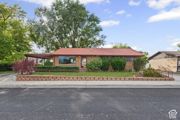 Brick exterior featuring a red metal roof, covered carport, and established landscaping