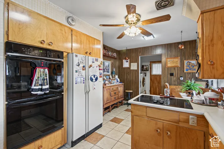 Built-in wall oven and cooktop, wood-finish cabinetry, ceiling fan with integrated lighting, and checkered floor tiling