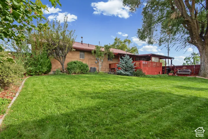 Expansive green lawn with mature trees and a multi-level deck featuring a covered patio