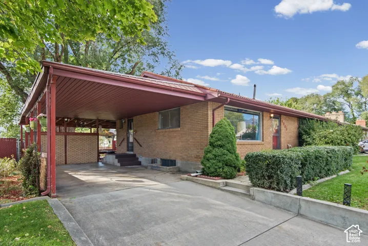 Brick exterior with an attached carport, covered entry, front door, and established landscaping
