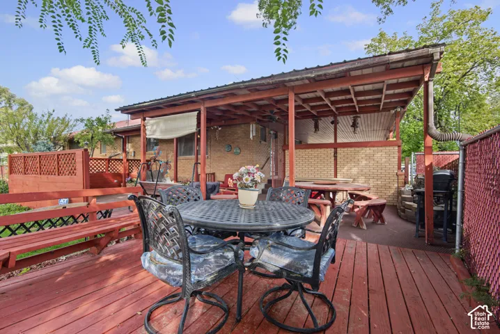 Expansive wooden deck featuring a built-in bench, covered patio, and brick exterior