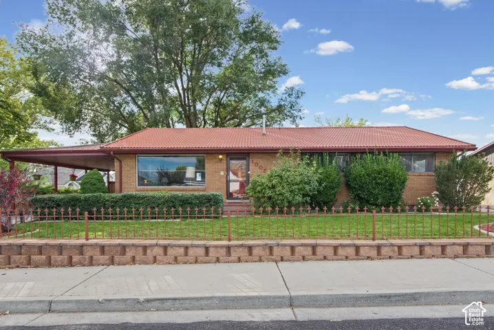 Brick exterior with a red tile roof, featuring a carport, front yard landscaping, and a decorative metal fence