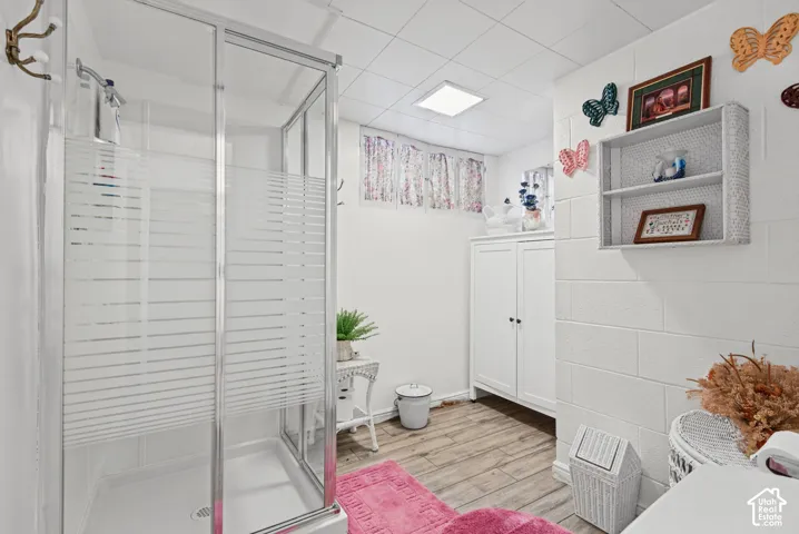 Enclosed shower with frosted glass, wood-finish flooring, white built-in cabinetry, and white block walls