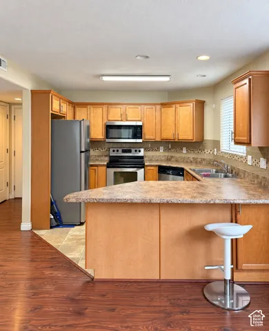 Kitchen featuring wood cabinetry, wrap-around laminate countertops, stainless steel appliances, tiled backsplash, and wood-finish flooring