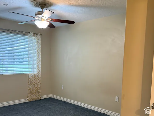 Interior space featuring neutral wall paint, dark wall-to-wall carpeting, a ceiling fan with integrated light fixture, and horizontal window blinds