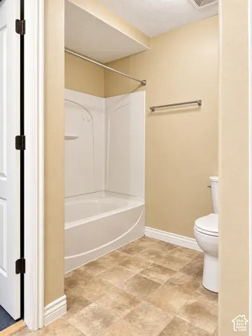 Bathroom featuring a white molded tub and shower surround, a porcelain toilet, and neutral-toned tile flooring