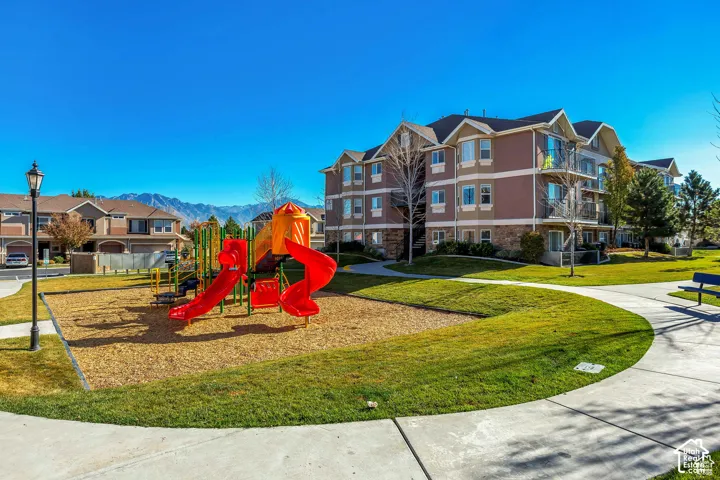 Common area featuring a playground with a slide structure, mulched ground cover, manicured lawn, paved pedestrian pathways, and mountain backdrop