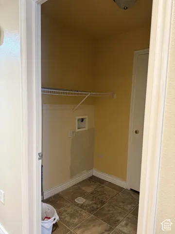 Utility closet featuring tile flooring, a wall-mounted wire storage shelf, and dedicated water and electrical hookups