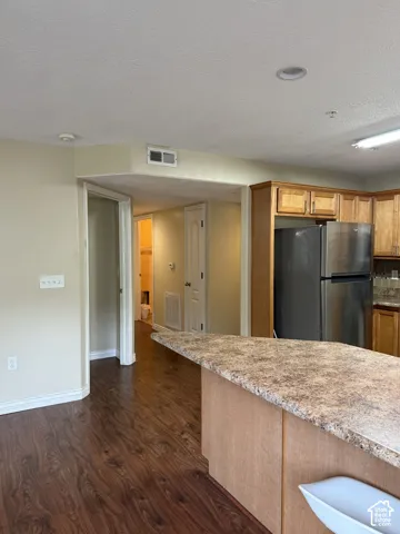 Kitchen featuring wood-finish cabinetry, stone-finish countertops, wood-finish flooring, and a stainless steel refrigerator