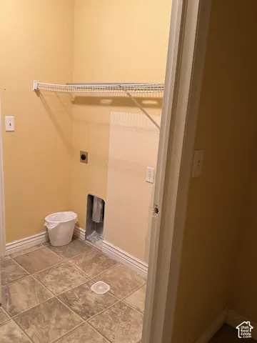 Utility area featuring tile flooring, a wall-mounted wire storage shelf, and dedicated plumbing and electrical hookups