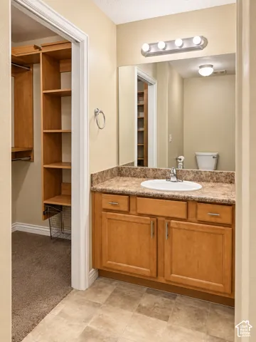 Vanity featuring wood cabinetry, solid surface countertop with integrated oval sink, four-light fixture, wall-to-wall mirror, and built-in closet shelving