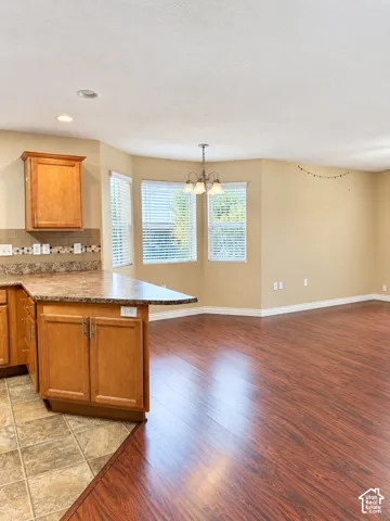 Kitchen area featuring wood cabinetry, stone-patterned countertops, tile backsplash, wood-finish flooring, and a multi-light chandelier
