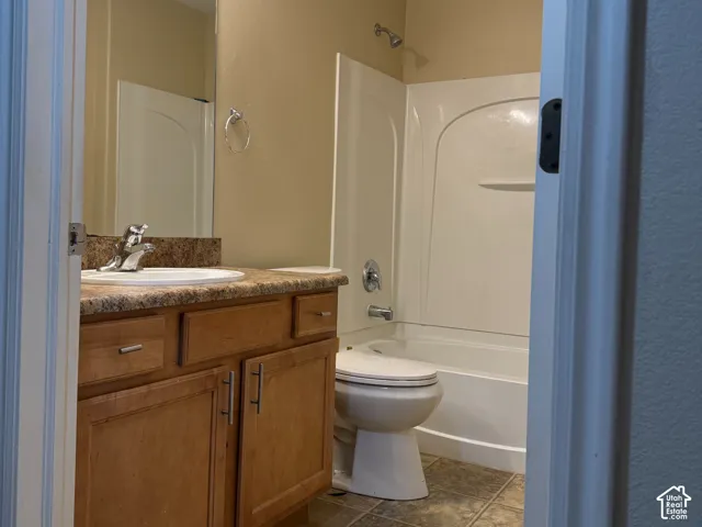 Bathroom featuring wood-finish cabinetry, stone-patterned countertop, integrated basin, tile-finish flooring, and a combined tub and shower surround