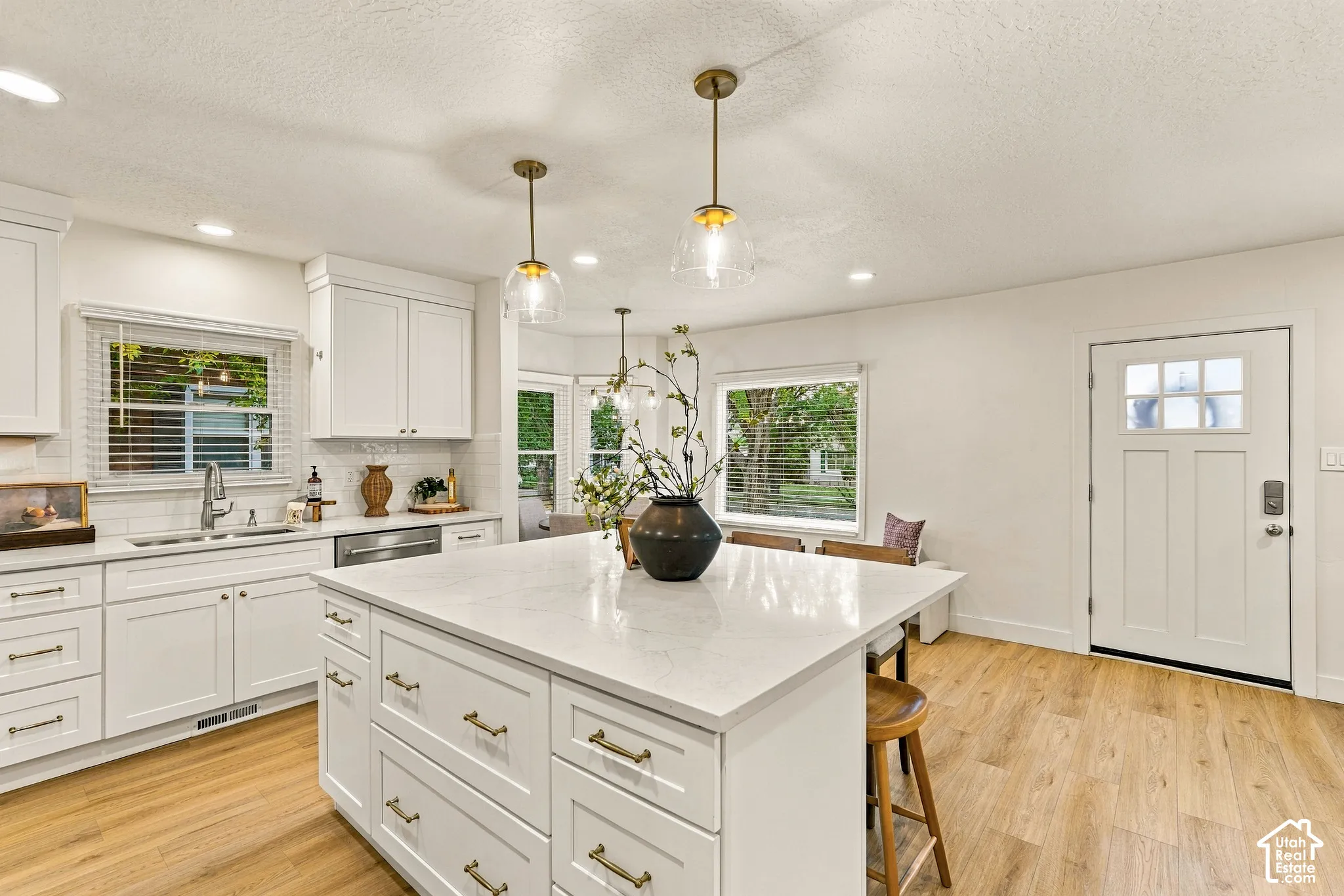 White cabinetry with brass hardware, a large kitchen island with a light-toned countertop, wood-finish flooring, and recessed lighting
