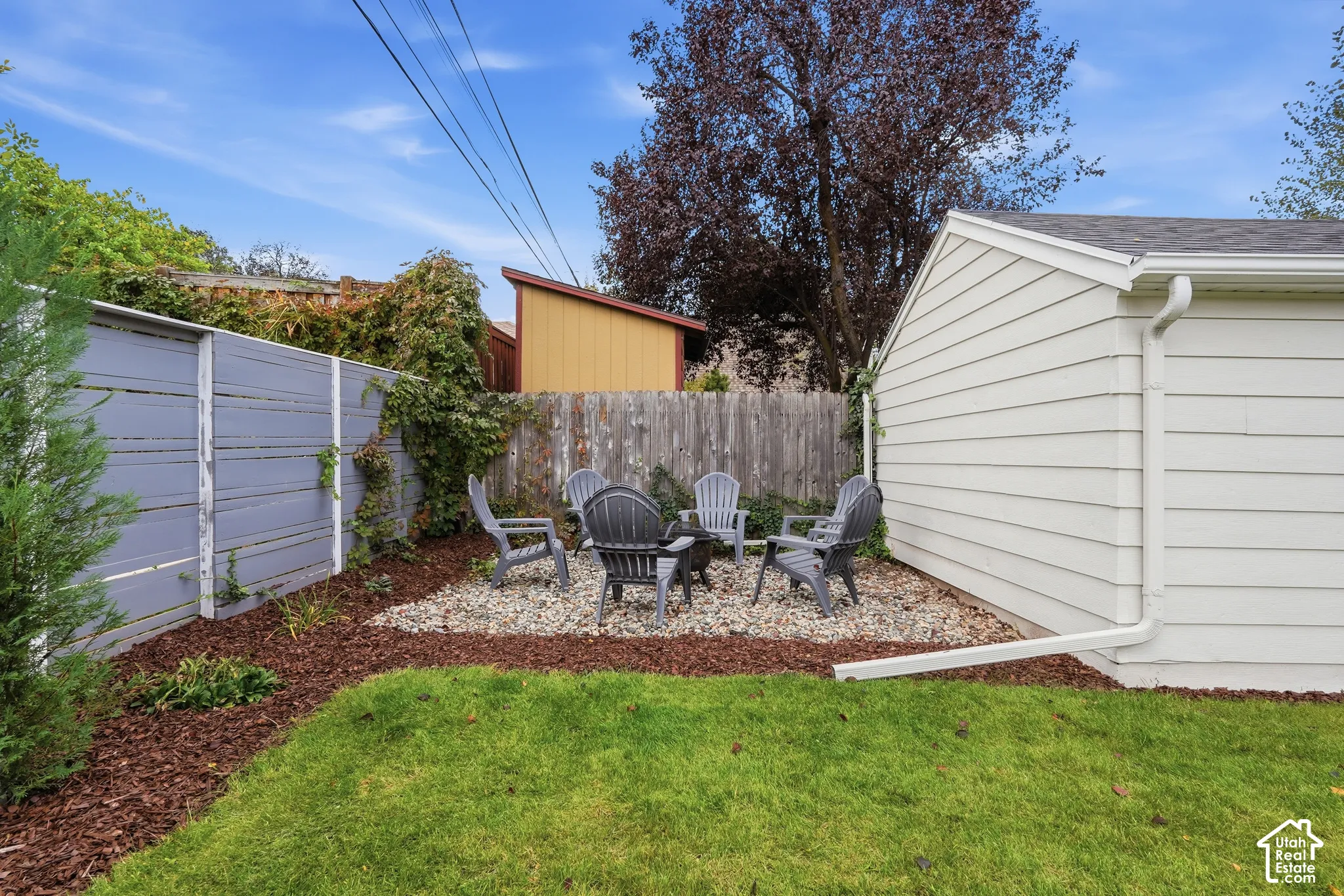 Backyard featuring a gravel patio area, wood chip landscaping, and a slatted privacy fence