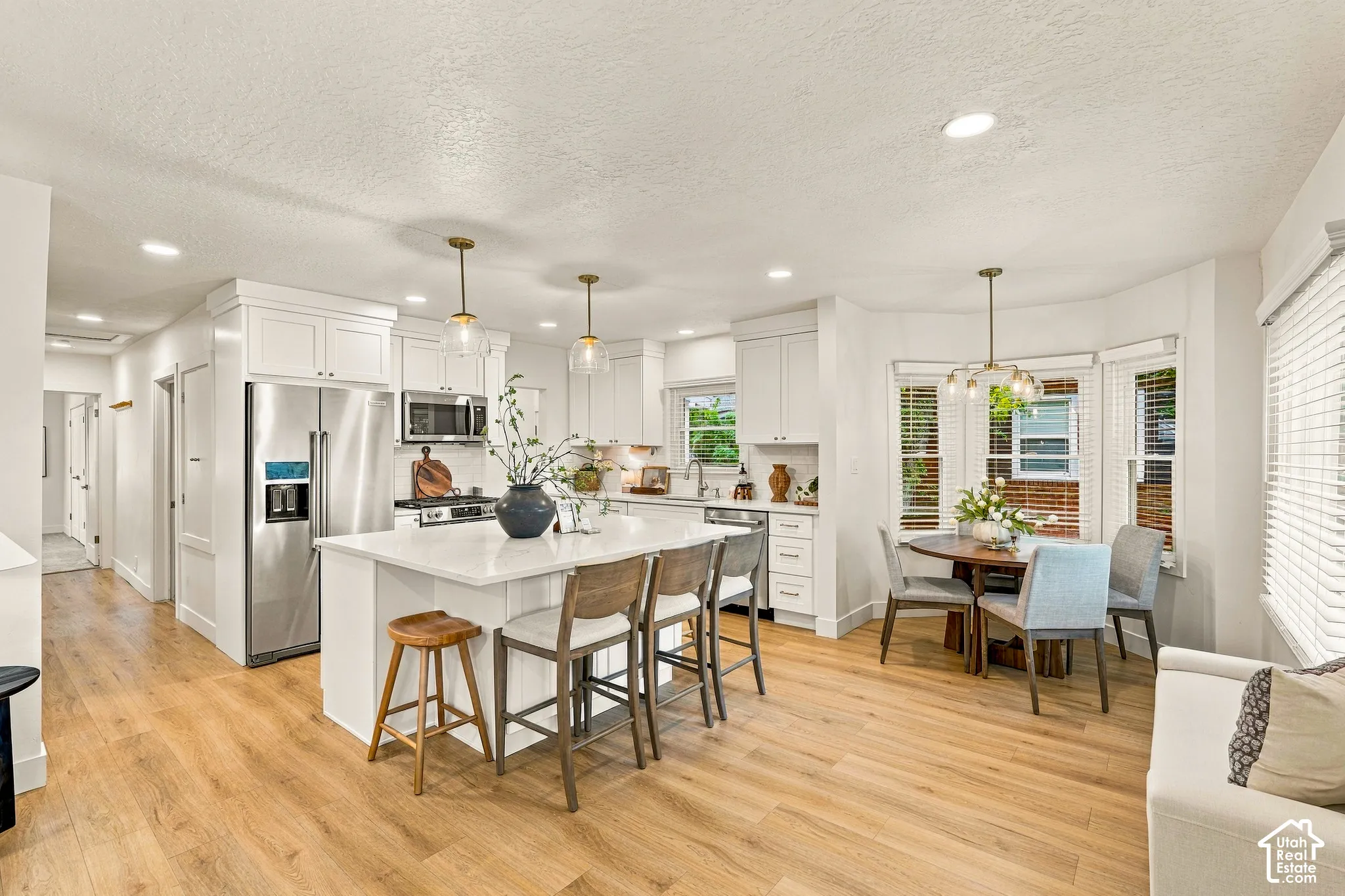 Open-concept kitchen featuring white cabinetry, stainless steel appliances, a center island with seating, and wood-finish flooring